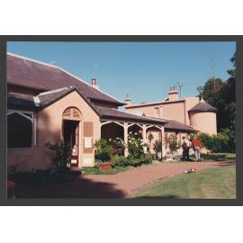 Western (front) entrance with verandahs, Turret room, and two - storey extension. Open day