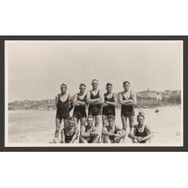 Bathers, group of men in bathing costumes, 5 standing, 4 sitting. At Bondi beach. Hotel Astra in background on right.