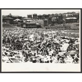 Bathers on beach, North Bondi, beach Umbrellas. Raffles Hotel and 'beach court' in background.