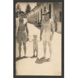 Bondi beach, two men with a child beside Bondi Pavilion. Note barbed wire of World War II at right.
